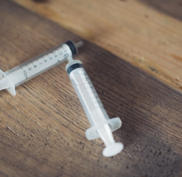 white and black plastic syringe on brown wooden table